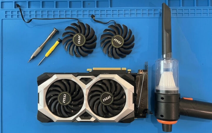 MSI graphics card with both cooling fans removed for replacement, laid out on an anti-static repair mat with screwdrivers and a dust blower